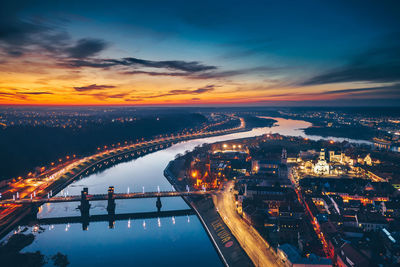 Aerial view of illuminated bridge over river in city at sunset