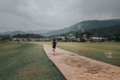 Rear view of boy playing with bubbles amidst field on footpath