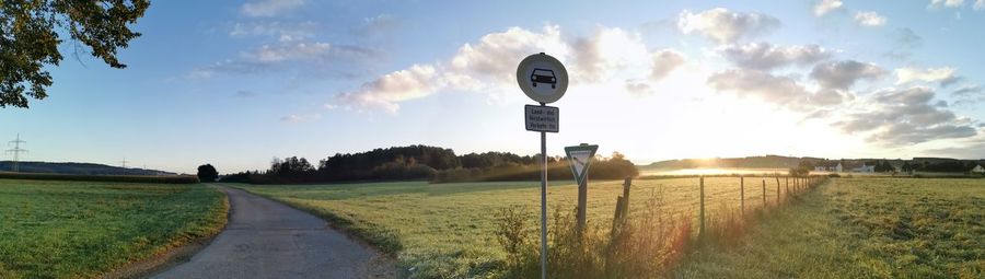 Road sign on field against sky