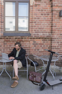 Man with electric scooter sitting at pavement cafe using laptop