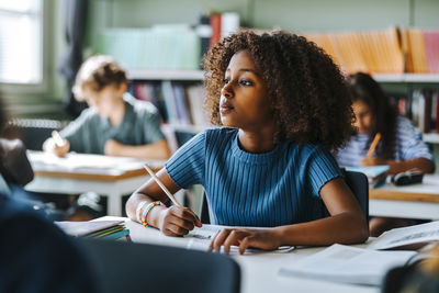 Thoughtful curly hair girl sitting near desk in classroom at elementary school