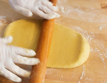 A dough is rolled with a rolling pin during the preparation of a cake. two hands with  gloves moving