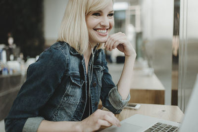 Happy woman using laptop computer while sitting by window in cafe