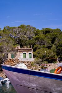 Boats moored by trees against blue sky