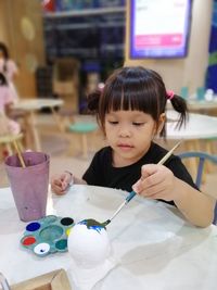 Girl painting figurine at table in classroom