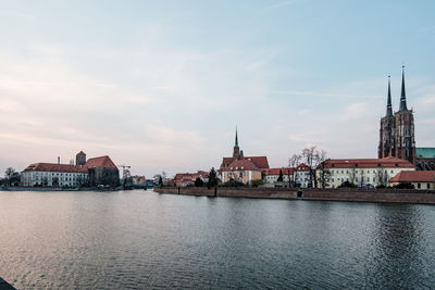 View of buildings by river against sky in city