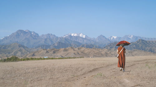 Rear view of woman walking on mountain against clear blue sky