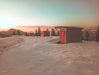 Scenic view of a cottage in snow against sky during sunset