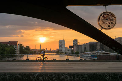 Man riding bicycle on bridge over river in city