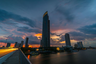 Skyscrapers by chao phraya river against cloudy sky