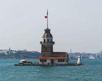 Lighthouse by sea against buildings against clear sky