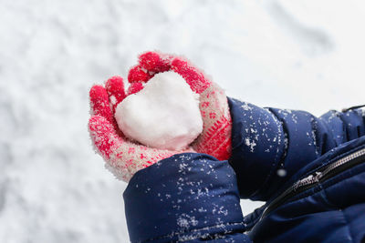 Child girl holding creative snowball in heart shape. female hands in pink wool mittens heart snow 