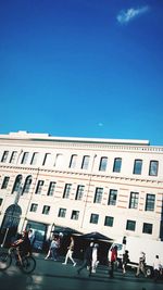 People on street by building against blue sky