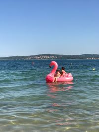 Boy and girl playing in sea against clear sky