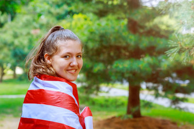 Portrait of smiling teenage girl with american flag against trees