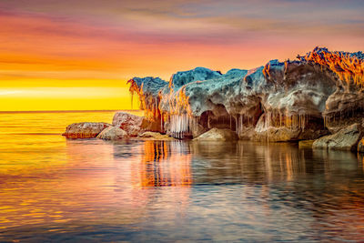 Rock formation in sea against sky during sunset