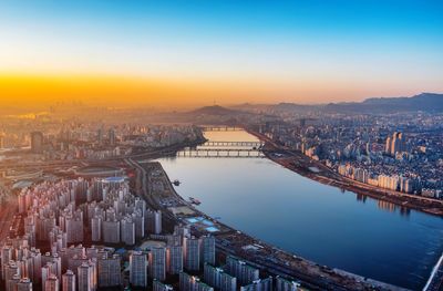 Aerial view of river amidst buildings in city during sunrise
