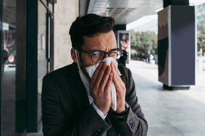Sick man with protective face mask coughing and sneezing on street.