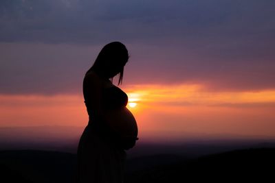 Side view of silhouette pregnant woman standing against orange sky