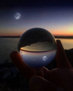 Close-up of hand holding crystal ball against sea at sunset