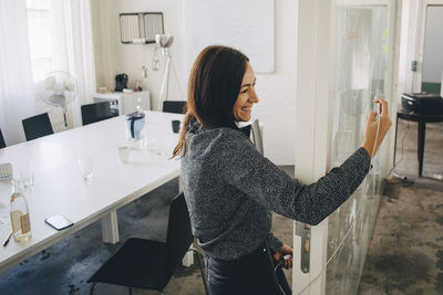 Smiling creative businesswoman taking selfie while standing at doorway of board room