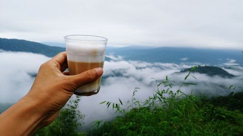 Midsection of person holding drink against sky