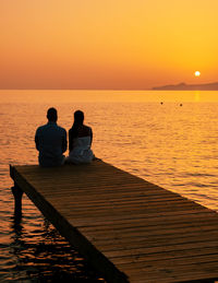 Rear view of man walking on pier against sea during sunset