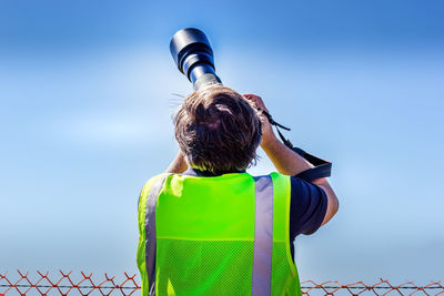 Rear view of man photographing against blue sky