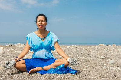 Portrait of young woman sitting on beach against sky