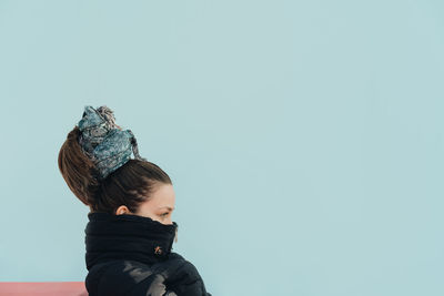 Close-up of woman wearing turtleneck jacket against wall