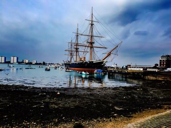 Boats in harbor against cloudy sky