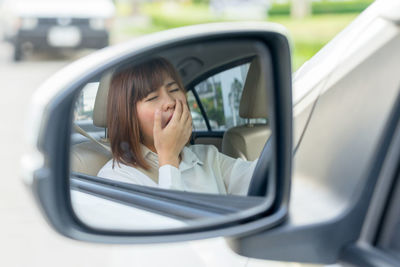Reflection of woman yawning in side-view mirror of car