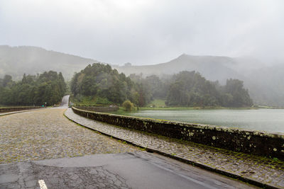 Road by trees against sky during rainy season