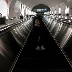 Low angle view of woman sitting on escalator at subway station