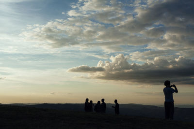 Silhouette people standing on land against sky during sunset