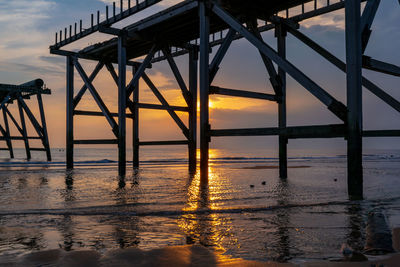 Reflection of pier on sea against sky during sunset