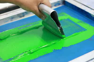 Cropped hand of person applying green ink on silk screen while working at workshop