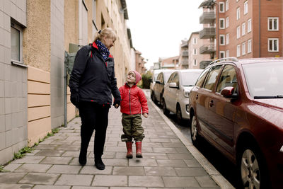 Full length of grandmother and grandson in warm clothing walking on footpath in city