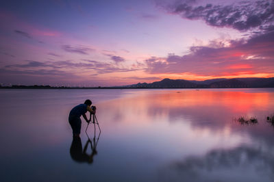 Man photographing while standing in lake during sunset