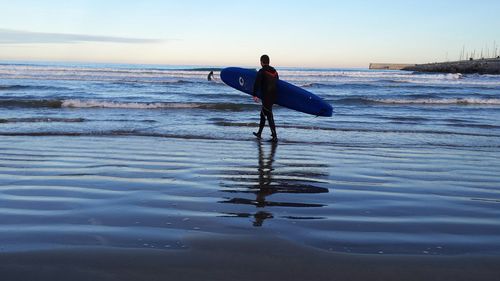 Man carrying surfboard walking on sea shore