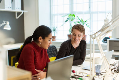 Smiling multi-ethnic female professionals working at illuminated desk in creative office