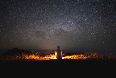 Rear view of man standing on field against sky at night