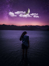 Rear view of woman standing against sky at night