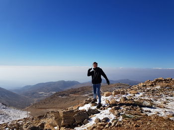 Full length of man holding snow while standing on mountain against clear blue sky