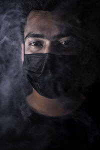 Portrait of young man wearing mask amidst smoke