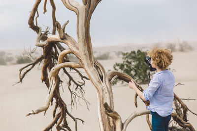 Man standing on tree at beach against sky