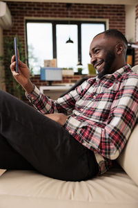 Young man using mobile phone while sitting on bed at home