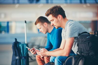 Friends using phones while waiting at airport departure area