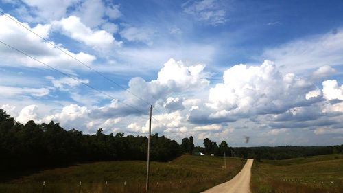 Road passing through field against cloudy sky