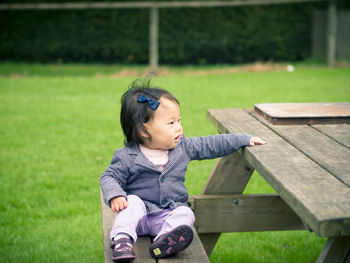 Baby girl looking away while sitting on picnic table outdoors